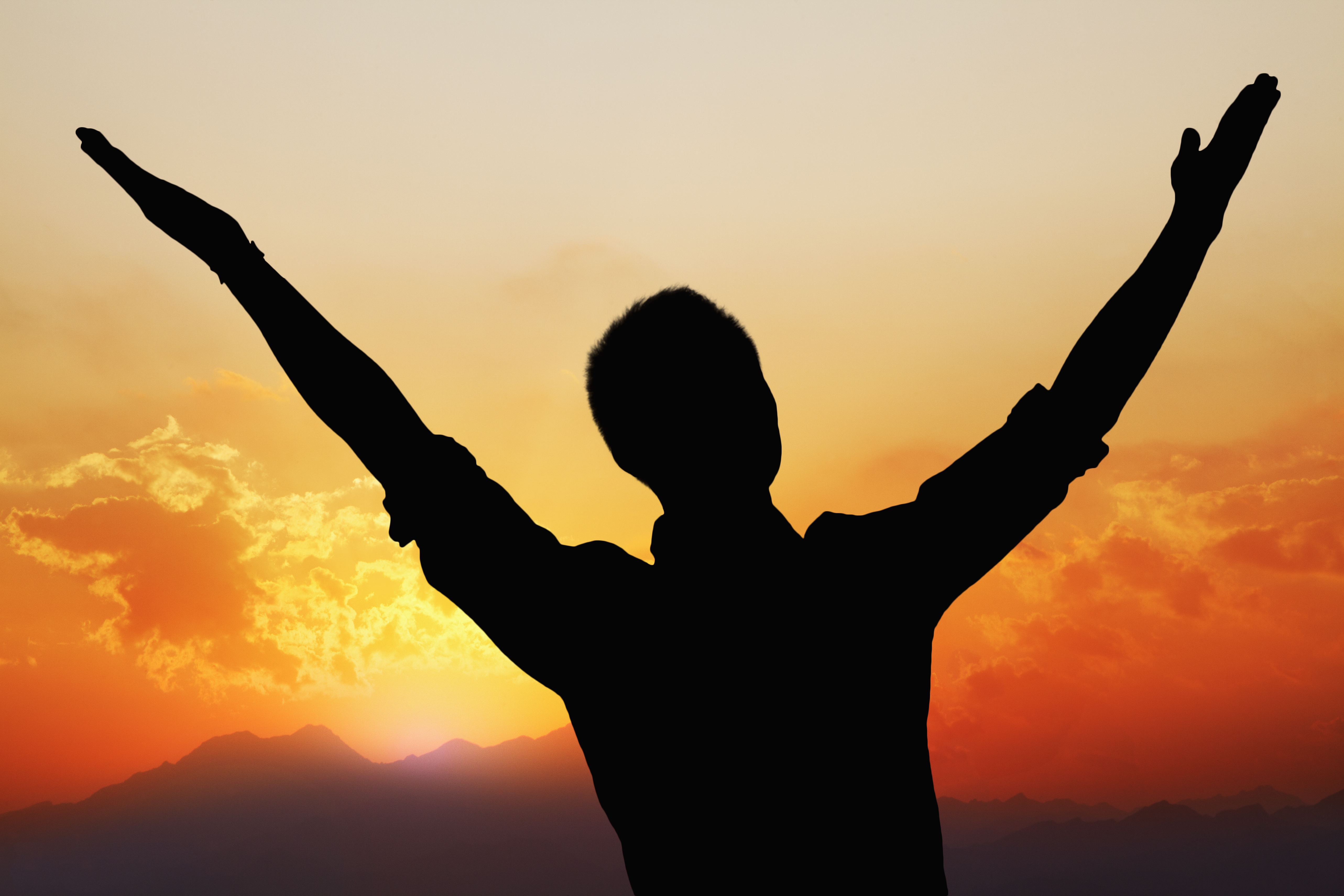 Silhouette of a man with arms raised high with a beautiful sunset and landscape in the background