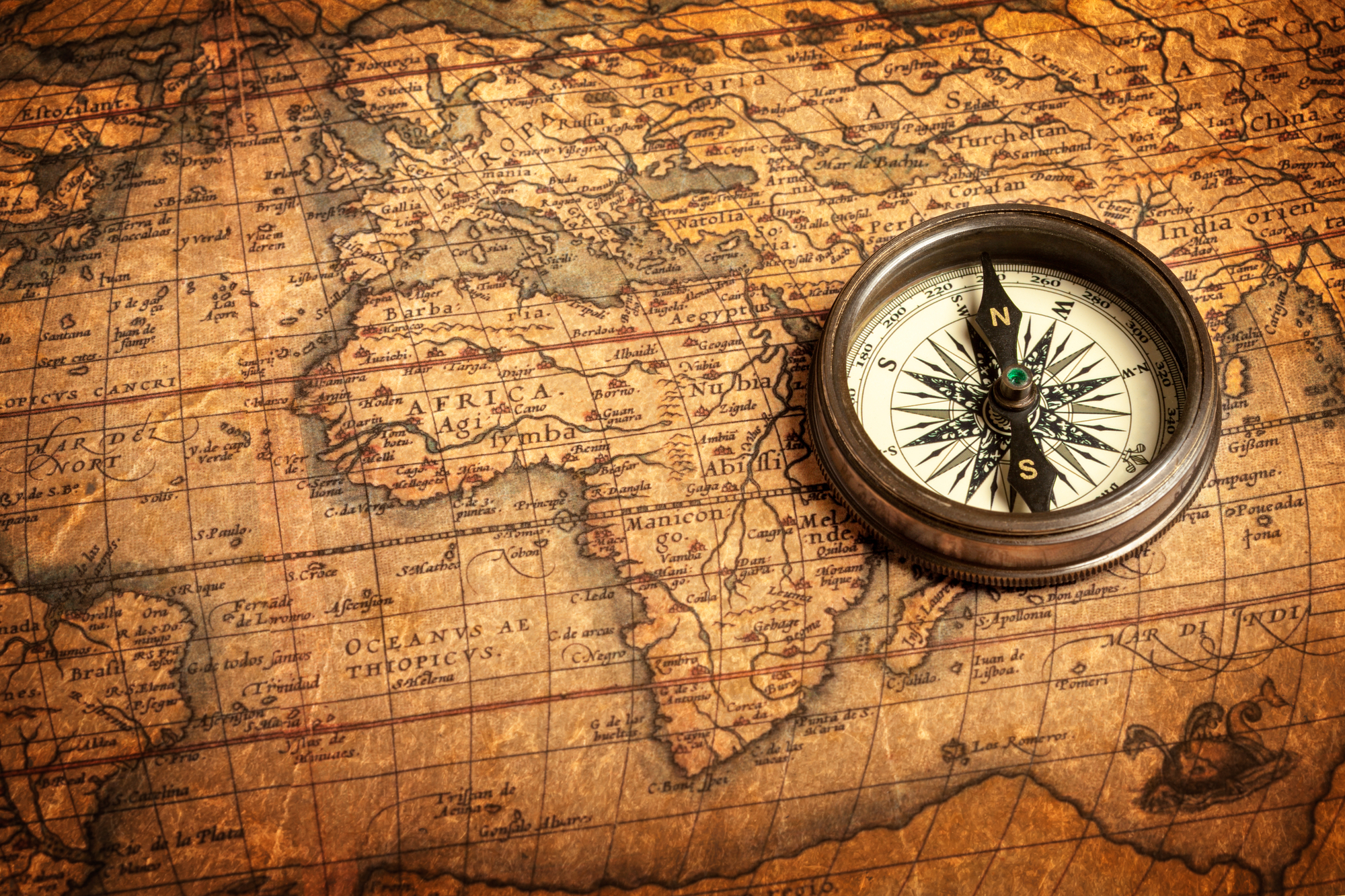 An antique compass rests on an old map of countries on planet Earth