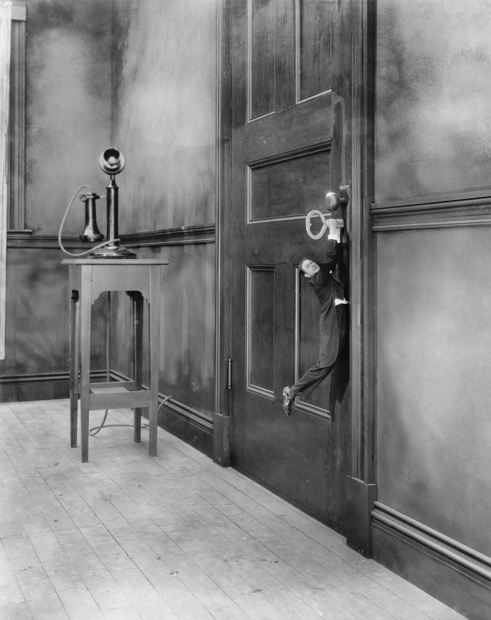 Black & White of tiny man hanging onto a key stuck in a locked door a la Alice in Wonderland
