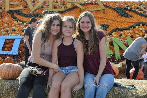 Young, smiling girls, are sitting with pumpkins in the background on a pumpkin festival