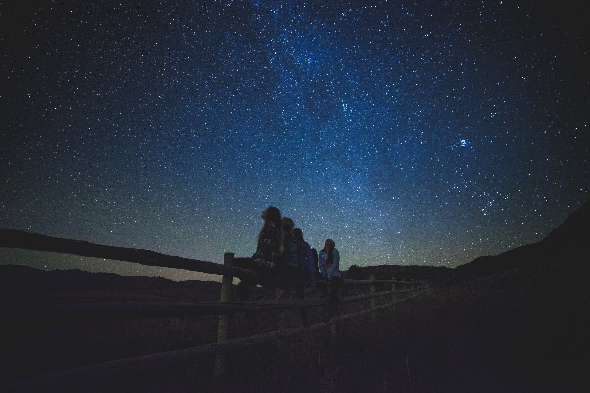 Stargazing girls in the night below the dark blue sky