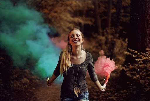 A blond girl with colorful smoke bombs in her hands