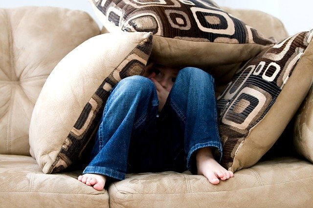 Little boy fearful under a shelter made from pillows