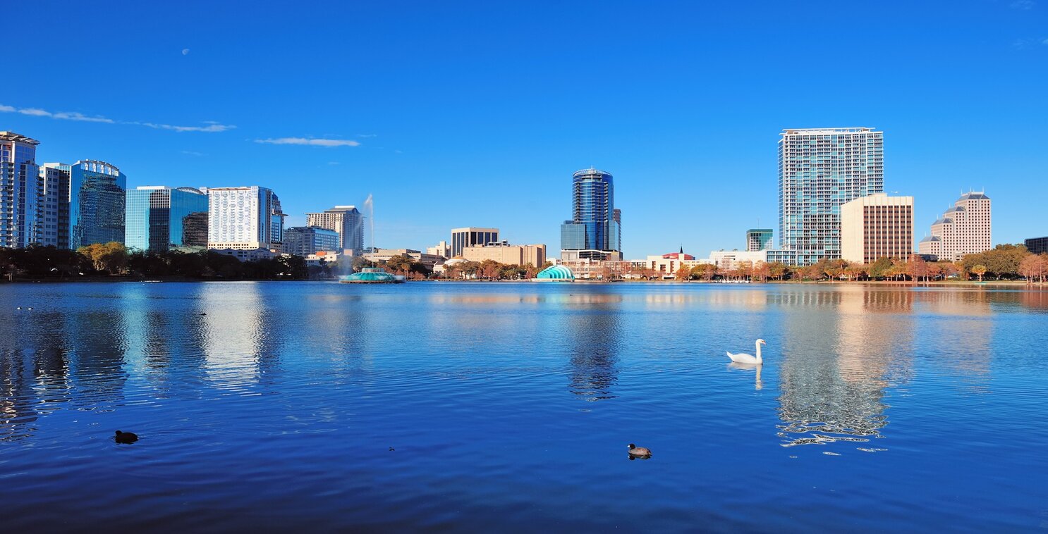 View of Orlando lake with urban skyscrapers and clear blue sky with swans.